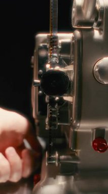 Eski bir film projektörünü çalıştıran bir elin yakın çekimi, lensten parlayan parlak bir ışık, klasik sinemanın nostaljik bir parıltısını yansıtıyor.
