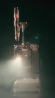 Eski bir film projektörü, objektifinden, atmosferik dumanla birlikte parlak bir ışık huzmesi yayar ve nostaljik bir sinematik ortam yaratır.