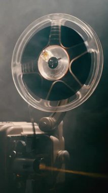 Eski bir projektörde dönen bir film makarası titreyen ışık ve ince dumanla nostaljik bir sinema havası yaratıyor.