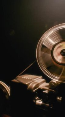 Elle çalışan bir retro film projektörünün yakın çekimi, makaranın mekanik hareketini ve klasik sinema ekipmanlarını iş başında gösteriyor.
