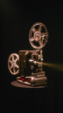 Bir Bolex M8 klasik film projektörüne yaklaşırken, parlak mercek ışığı karanlık bir iç mekânda parlıyor ve klasik retro sinema ekipmanlarını vurguluyor.
