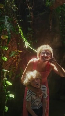 Bir kadın ve bir çocuk, yemyeşil bir bahçede huzur dolu bir anı paylaşıyor. Kelebeklerin uçuşunu izlerken gözleri merakla parlıyor.