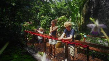 Çocuklar renkli tropikal bitkilerle dolu canlı bir kelebek sığınağını keşfeder ve etraftaki kanat çırpan kelebeklerden zevk alır ve hayrete düşerler.