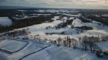 Dağınık ağaçlarla kaplı açık karlı bir parkın insansız hava aracı görüntüsü, yukarıdan huzurlu bir kış atmosferini yakalıyor.