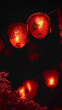 Çin Mahallesi 'nde canlı bir kültürel gece gösterisi. Parlak kırmızı fenerler ve akşam gökyüzünün altında süslü kiraz çiçekleri.