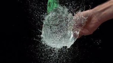 Yeşil bir su balonunun yavaş çekimde iğne temasında aniden patlaması, suyun siyah bir arka plana sıçraması.