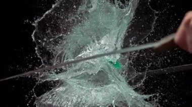 Çifte kılıç darbesinden patlayan yeşil su balonunun dramatik bir yavaş çekimi. Siyah arka planda su fışkırıyor.