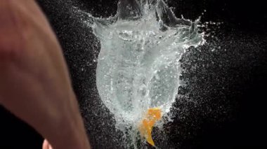 Bıçak, sarı su balonunu yavaş çekimde kesiyor ve siyah arka planda dramatik bir su patlamasına neden oluyor.