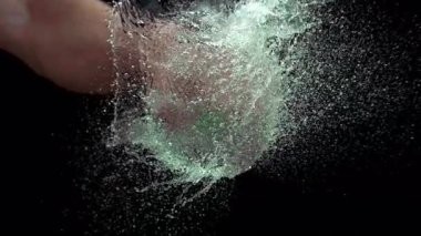 Bir yumruk, yeşil su balonunu yavaş çekimde yumrukluyor ve siyah arka planda patlayıcı bir sıçramaya neden oluyor.