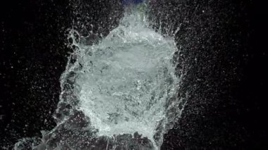 Bir kılıç mavi su balonunu yavaş çekimde keser, dramatik bir su patlaması yaratır ve siyah bir zemine doğru yüzen parçacıklar bırakır.