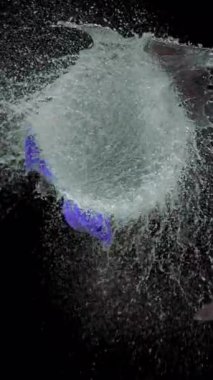 Bir bıçak menekşe su balonunu yavaş çekimde keser ve siyah arka plana çarpan çarpıcı bir patlama ve detaylı sıçrama efektini ortaya çıkarır.