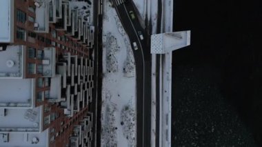 Bir kış manzarası karla kaplı bir konut alanı yakalar, binalar, hareketli arabalarla dolambaçlı yollar ve çarpıcı liman manzarası