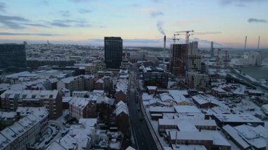 Bu hava aracı görüntülerinde karla kaplı çatılar ve sokaklar, modern yüksek binalar, aktif inşaat vinçleri ve araç trafiği olan merkezi bir yol yer alıyor.