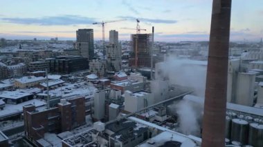 Karla kaplı bir şehir bölgesinin huzurlu kuş bakışı görüntüsü devam eden inşaat, hareket eden trafik ve kış güneşinin ince parıltısını vurguluyor.