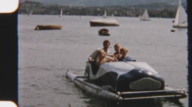 Bir baba ve çocuklarının sakin sularda yüzen yelkenlilerle çevrili bir pedal teknesinde keyif aldıkları ve keşfettikleri keyifli bir günü yakalayan klasik bir 8 mm film.