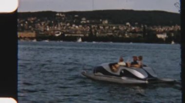 Kardeşler neşe içinde bir tekneyi sakin bir gölde gezdirirler. Etrafı yemyeşil tepelerle çevrilidir. Arka planda büyüleyici bir şehir vardır.