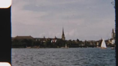 Sakin bir 8 mm 'lik film, sakin bir göl kenarında seyreden yelkenlileri yakalıyor, büyüleyici miras binaları tarafından çerçeveleniyor.