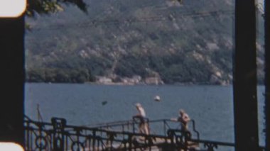 8mm 'lik klasik görüntüler, parlak bir günde, gölün manzarasına bakan, rıhtımdaki korkulukların yanında duran çocukları gösteriyor.