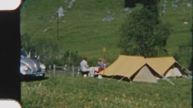 8 mm 'lik görüntüler, kadınların manzaralı bir vadide çadırda dinlenirken, yakınlarda klasik bir Volkswagen Beetle park halindeyken, zamansız bir kamp anını anımsattığını gösteriyor.