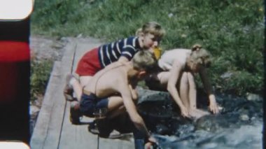 8 mm 'lik bir filmde çocuklar nehrin kenarında oturur, huzurlu ve doğal bir ortamda neşeyle tatlı su içerler.