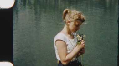 8 mm 'lik bir film, arka planda karlı bir dağ sırası olan manzaralı bir gölün yanında kır çiçeklerini tutan genç bir kızın görüntüsü.