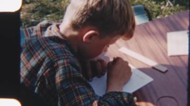 8 mm 'lik film, doğanın ortasında, ağaçlar ve huzurlu yeşilliklerle çevrili ahşap bir masada yazılı bir çocuk görüntüsü.