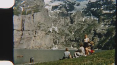 İsviçre Alpleri 'ndeki Oeschinen Gölü' nde dinlenen ve manzaranın keyfini çıkaran bir ailenin dağlarla çevrili 8 mm 'lik görüntüsü.