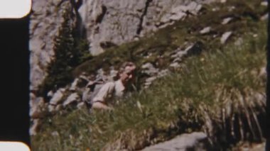 8mm 'lik bir ailenin parlak güneş ışığı altında yemyeşil bitki örtüsüyle çevrili kayalık bir dağ yolunda yürüdüğünü gösteren görüntüler.