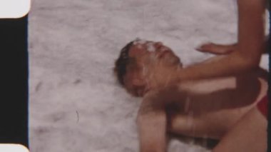 8 mm 'lik film, açık havada karlı bir aile ortamında babasının yüzünü karla kaplayan oyuncu bir kızın görüntüsü.