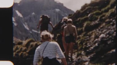 8mm 'lik bir film, engebeli dağ zirvelerinin dramatik zeminine sahip manzaralı bir patika boyunca kuyrukta yürüyen bir aileyi gösteriyor.