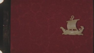 8mm 'lik stop motion animasyon klipindeki bu çerçeve, zengin kırmızı, dokulu bir zemin üzerinde süzülen, ince film tahılı ve organik hareketle stilize edilmiş beyaz yelkenli bir gemiyi gösteriyor.