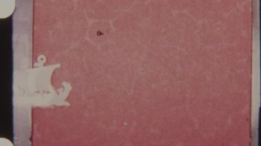 Klasik bir 8mm stop motion klipte iki küçük beyaz yelkenli gemi düz kırmızı bir zemin üzerinde yatay olarak hareket eder, görünür sivri uçlu delikler ile kumlu, retro ve deniz hissi yaratır.