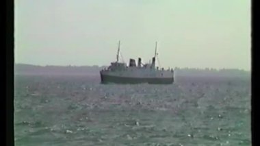 Vintage VHS footage shows a white passenger ship with twin smokestacks sailing across rippled waters against a faint shoreline backdrop