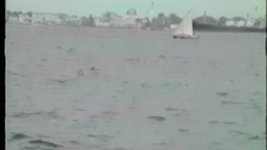 This VHS footage shows a small sailboat gliding across choppy waters in South Korea, framed by larger docked ships and a distant skyline with domes and spires