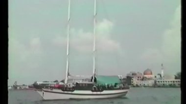 A classic wooden yacht drifts along the coast of South Korea, its twin masts and canopy-covered deck captured in nostalgic camcorder style