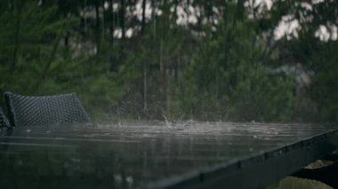 A static shot showing outdoor synthetic wood furniture in rain with lush green garden background