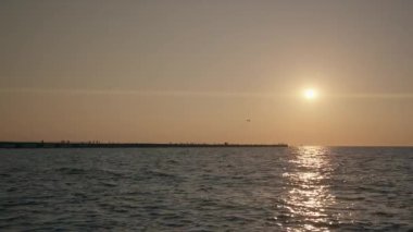 Static shot of calm ocean waves rolling gently as sunset light dances on the surface, creating a peaceful golden seascape