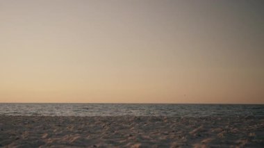 Romantic couple walking along the shoreline with rolling waves and a vibrant sunset sky in the background