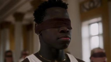 A young man with a serious expression wears a sheer blindfold, creating an intense and mysterious atmosphere