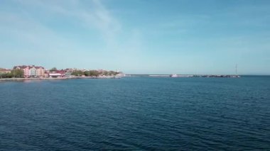 A small sea fishing port with boats in the calm deep cool Black Sea adjoins the ancient resort small town of Pomorie in Bulgaria, under a blue cloudy sky. UHD 4K video realtime