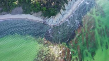 Unusual rocky seabed covered with transparent turquoise wavy water of the Black Sea near a sandy wild rocky beach with vegetation ledges and cliffs. UHD 4K video realtime