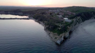 A small ancient resort town with expensive remote comfortable hotels on rocky outskirts, above a sandy vegetative wild beach near the deep blue Black Sea under a clear blue sky. UHD 4K video realtime