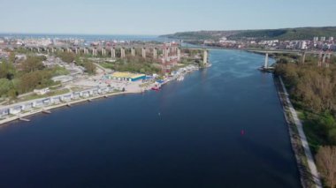 Large road bridge with trendy modern powerful cars passes over strait of Black Sea in ancient industrial city of Varna, with summer small hotels and inns and green spring parks. UHD 4K video realtime