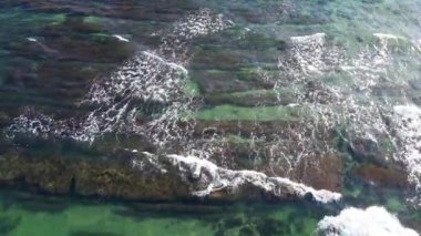 Unusual rocky seabed covered with transparent turquoise wavy water of the Black Sea near a sandy wild rocky beach with vegetation ledges and cliffs. UHD 4K video realtime