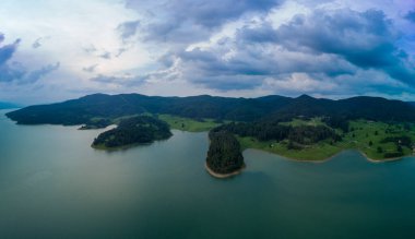 Dağlar arası göl, kıyıları bitki örtüsüyle kaplı Rodop dağları ve bulutlarının siluetlerine karşı. Panorama, üst manzara