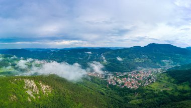 Evleri ve gölü olan küçük Bulgar kasabası Smolyan bulutların altında bitki örtüsü ve güneş ışınlarıyla kaplı. Rodop Dağları. Panorama, üst manzara