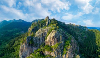 Rodop dağları vadisindeki bitki örtüsüyle yüksek dağların kayalık zirvesi ve geniş bulutlu gökyüzünün arka planına karşı ormanlar. Panorama, üst manzara