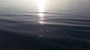 Boundless calm Black Sea with cool water reflecting light extends beyond the horizon, under colored sky with white volatile clouds and a bright dawn warm spring sun. UHD 4K video realtime