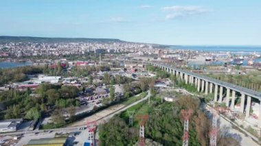 Large road bridge with trendy modern powerful cars passes over strait of Black Sea in ancient industrial city of Varna, with summer small hotels and inns and green spring parks. UHD 4K video realtime