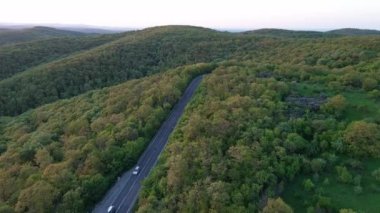 Hızlı modern araba ve kamyonlarla dolambaçlı yeni bir dağ yolu, ufuktaki yeşil yaprak döken ormanlarla Balkan Dağları arasındaki uzaklığa çıkıyor. UHD 4K video gerçek zamanlı